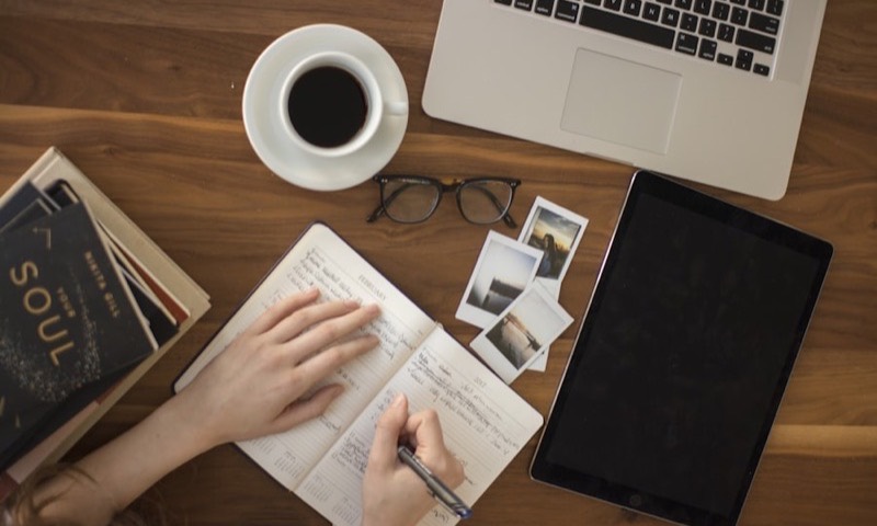 A weekly planner, laptop and coffee on a desk