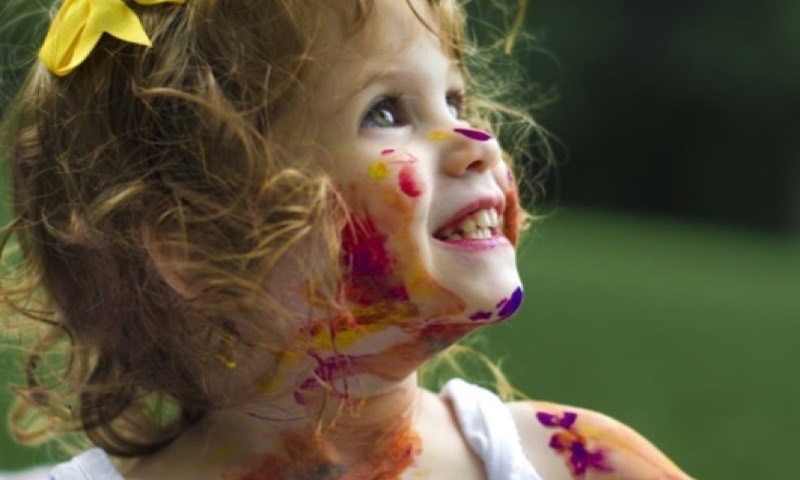 A little girl covered in paint, delighted with her work