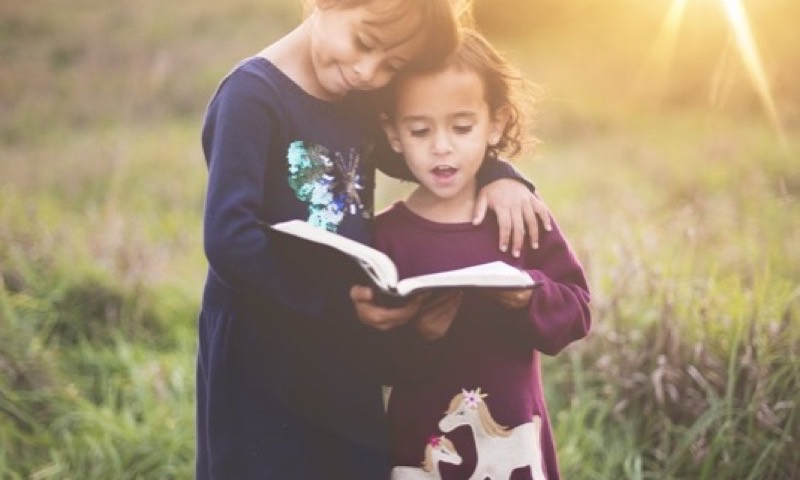 Two young sisters reading one book in golden evening light